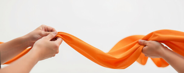 People pull two ends of an orange fabric in a bright setting during a creative activity in the afternoon light