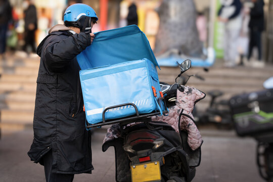 Delivery Worker Adjusting Blue Thermal Bag on Motorcycle