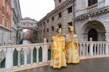 Two figures in golden Venetian carnival costumes and masks on a historic bridge in Venice. Concept of luxury travel, elegance and cultural heritage