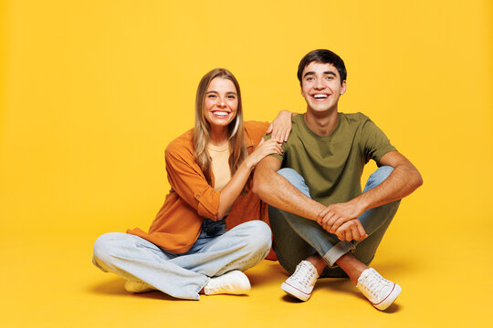 Full body smiling happy fun cheerful young couple two friends family man woman wear casual clothes together sitting look camera isolated on pastel plain light yellow color background studio portrait.