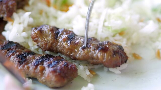 Close-up of grilled cevapcici served with rice and coleslaw, fork picks up one piece