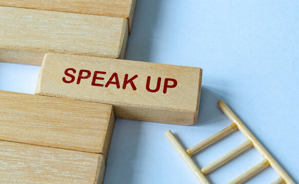 SPEAK UP text on wooden blocks with ladder representing accessible reporting and open dialogue.