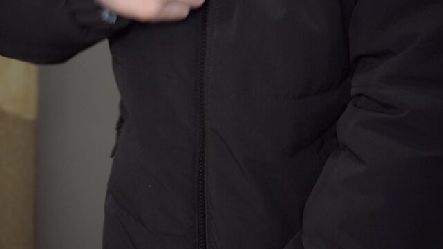man's hands holding zipper slider at bottom of jacket, guy puts on a black jacket close-up