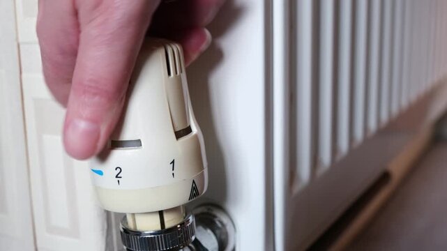 Close up of Hand Turning Down Thermostatic Radiator Valve from Five to Zero to Save Energy and Reduce Heating Costs. Cost of Living Crisis Household Savings.