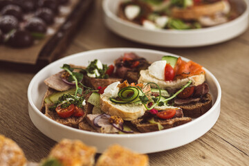 Assorted catering bruschetta with salmon, meat, and vegetables on a white plate.