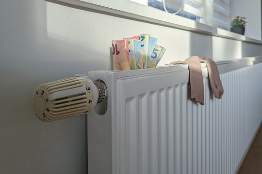 Radiator covered with euro bills shows poverty in Estonia, poverty limits warm homes, poverty pressure makes heating luxury. Baltic economy, charity messaging