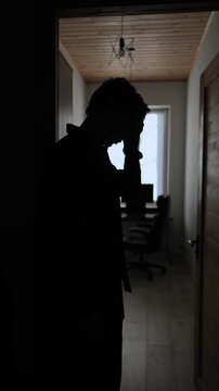 Man silhouette after losing job standing in doorway of home office, hand on forehead, shock and despair, unemployment crisis, freelancer lifestyle, vertical video