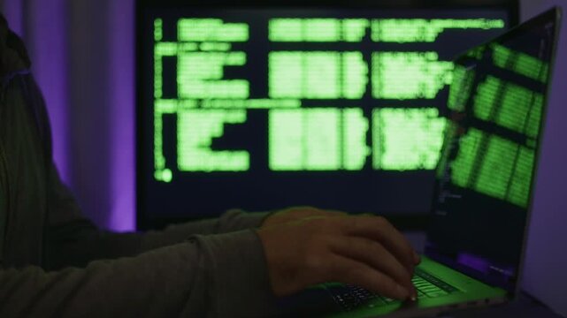 Coding in dim environment, User interacts with computer under moody lighting conditions, Operator inputs code commands on laptop while illuminated by purple light and monitors network activity