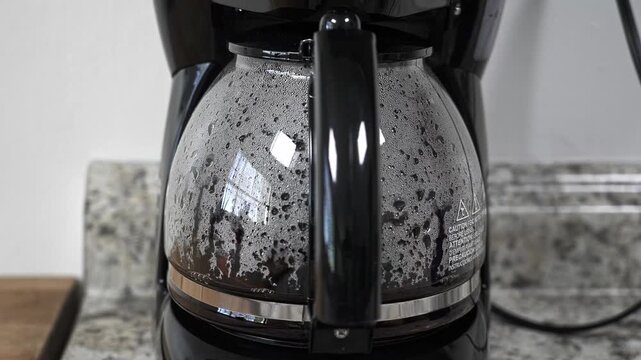Freshly brewed coffee filling a glass pot in an automatic drip coffee machine. A hot beverage preparing in a modern kitchen appliance