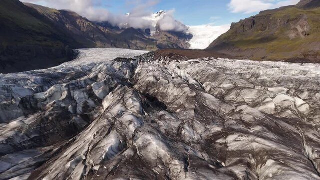 Aerial view of a vast glacier with rugged ice formations contrasting against dark mountains under a partly cloudy sky, Selfoss, Iceland.