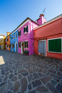 Colorful buildings with pink, blue, and orange facades under a clear blue sky. Burano, Venetian Lagoon, Italy