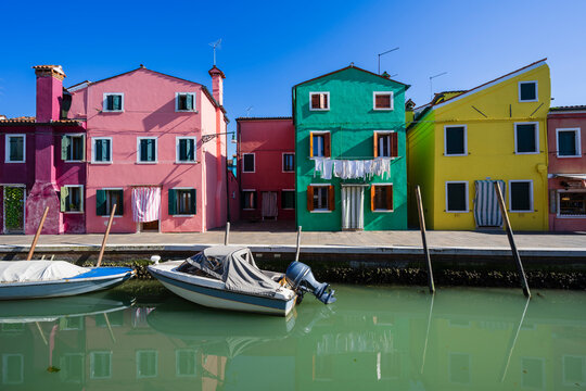 Colorful houses with hanging laundry reflect on a calm canal in a sunny day. Burano, Venetian Lagoon, Italy