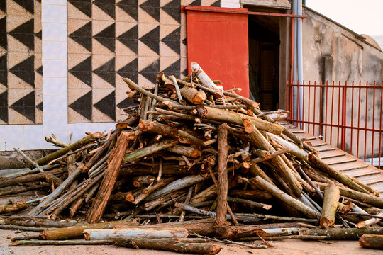 A pile of logs stacked in front of a geometric patterned building wall. Kigali, Rwanda
