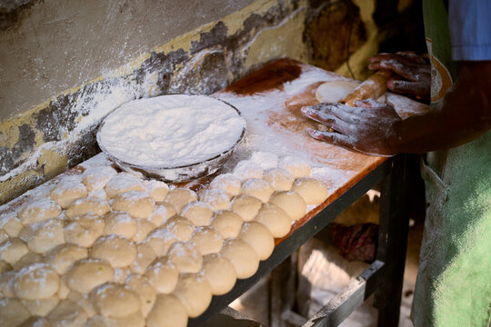 Hands work dough on a flour-covered wooden table with rows of dough balls. Kigali, Rwanda