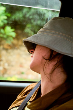 Woman wearing a hat and sunglasses sitting inside a car with greenery outside the window. Kigali, Rwanda
