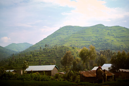 Verdant green hills with terraced farms under a partly cloudy sky near small rural buildings. Kigali, Rwanda