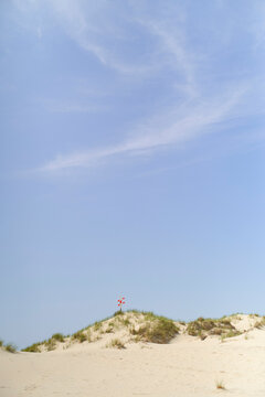 Sandy dunes under a clear blue sky with sparse clouds and a small sign on top. North Sea, Belgium