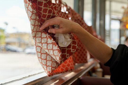 A hand opening a patterned orange curtain by a sunny window in a cafe. Miami, Florida, USA