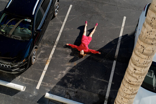 Woman in pink lies flat in empty parking space with arms and legs spread wide. Miami, Florida, USA