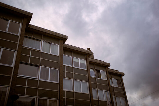 Overcast sky above a row of dark brown apartment buildings with large windows. Belgium