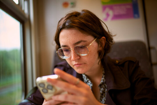 Person in glasses using a smartphone while traveling on a train. Belgium