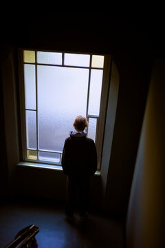 Person standing alone, back to camera, gazing through large frosted window. Germany