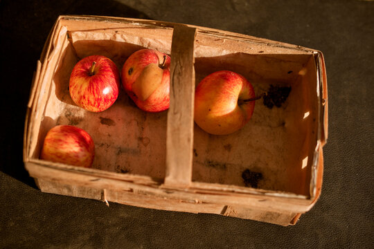 A wooden basket with red and yellow apples on a dark surface in warm lighting. Germany