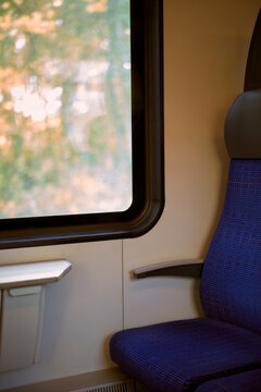 Train interior with a blue seat next to a large window showing blurred autumn scenery. Germany