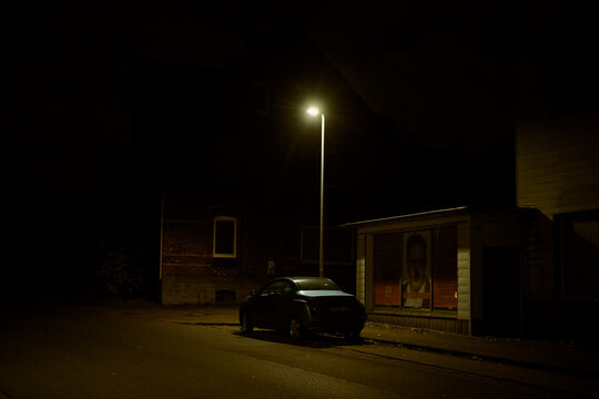 A car parked under a streetlight on a dark, quiet street at night. Germany