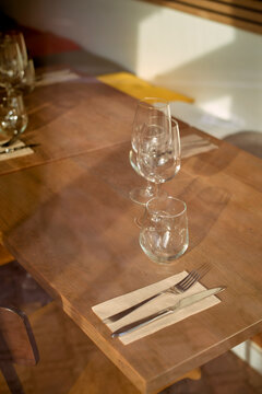 Sunlit wooden table set with wine glasses and cutlery in a cozy dining space. Belgium