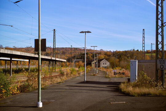 Abandoned train station platform surrounded by autumnal trees and clear blue sky. Germany