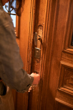 Person unlocking an ornate wooden door with detailed carvings and metal lock mechanisms. Belgium