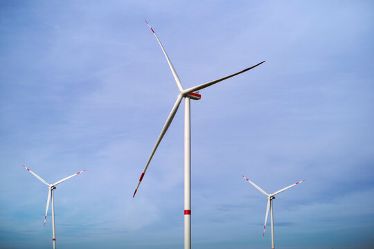 Three wind turbines stand tall against a blue sky with light clouds. Germany
