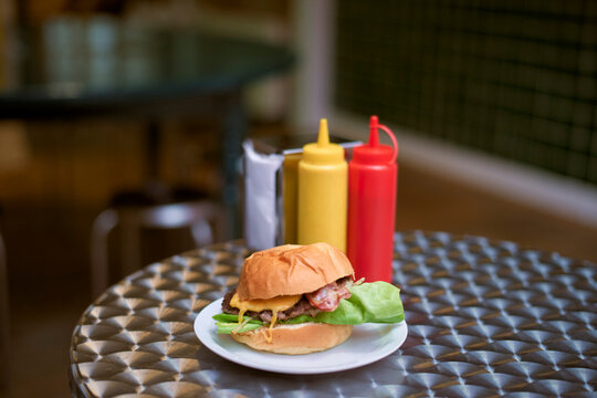 Juicy burger with lettuce and sauce on a metal table complemented by condiments. Belgium