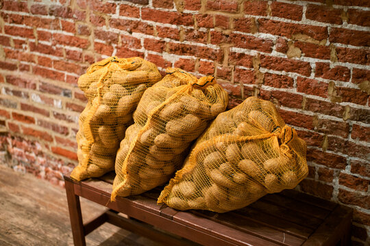 Three sacks of potatoes in yellow mesh bags on a wooden bench against a red brick wall Belgium