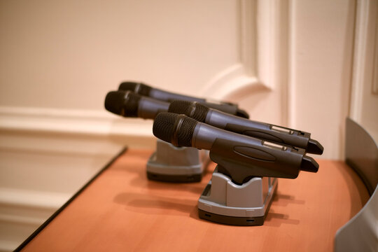 Three wireless microphones resting on a wooden desk in a well-lit room. Belgium