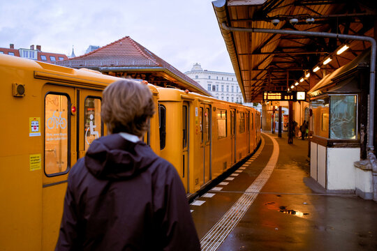 Person standing on train platform watching yellow train at urban station during evening. Germany