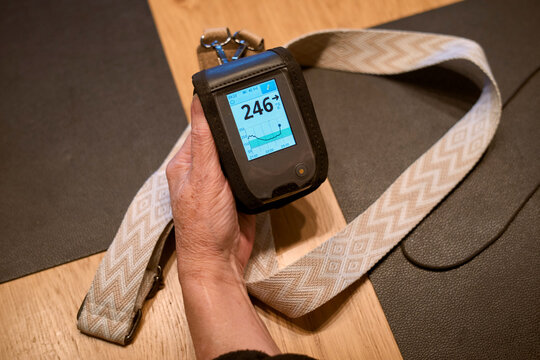 Hand holding a glucose monitor with a patterned strap on a wooden table. Germany
