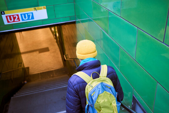 Person in vibrant winter attire descends green-tiled subway stairs toward platforms U2 and U7. Germany