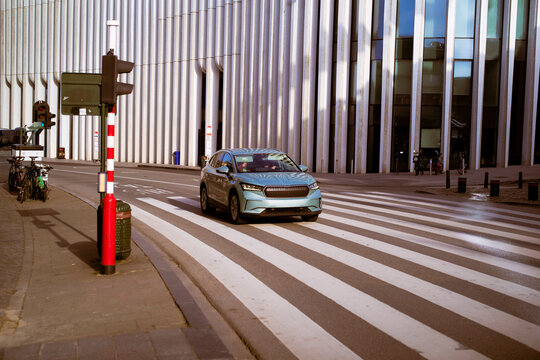Blue car driving on a city crosswalk near a modern building with vertical lines. Germany