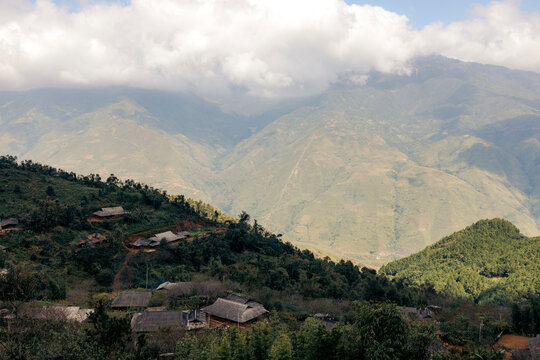Scenic view of lush green mountains and scattered traditional houses under a cloudy sky. Mountains of Ta Xua, Bac Yen District, Son La, Vietnam
