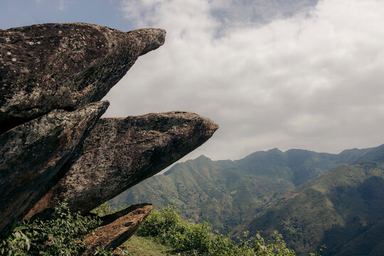 Rocky outcrop overlooking lush green mountains under a partly cloudy sky. Mountains of Ta Xua, Bac Yen District, Son La, Vietnam