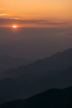 Sunrise over misty mountain range with vibrant orange sky and dark silhouette. Mountains of Ta Xua, Bac Yen District, Son La, Vietnam