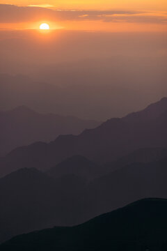 Sun setting behind the misty silhouette of layered mountain ridges under a golden sky. Mountains of Ta Xua, Bac Yen District, Son La, Vietnam