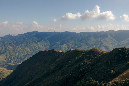 Rolling green mountains under a blue sky with scattered clouds in a scenic landscape view. Mountains of Ta Xua, Bac Yen District, Son La, Vietnam