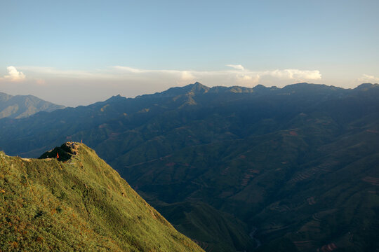 Rolling green mountains under a clear blue sky at sunset with distant peaks in the background. Mountains of Ta Xua, Bac Yen District, Son La, Vietnam