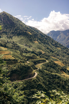 Lush green mountains with a winding road under a partly cloudy blue sky. Muong Te District, Lai Chau, Vietnam