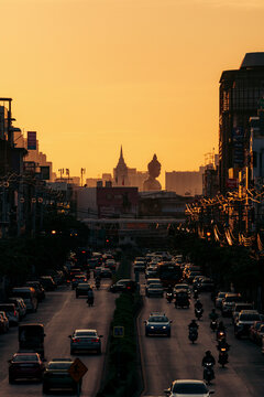 City street with heavy traffic at sunset, silhouetted Buddha, skyline and orange sky. Bangkok, Thailand