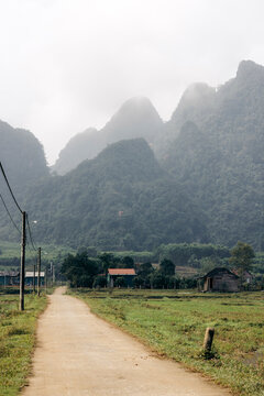 A dirt road leads to a rural village with misty mountains in the background. Minh Hoa, Quang B&Iuml;nh, Vietnam