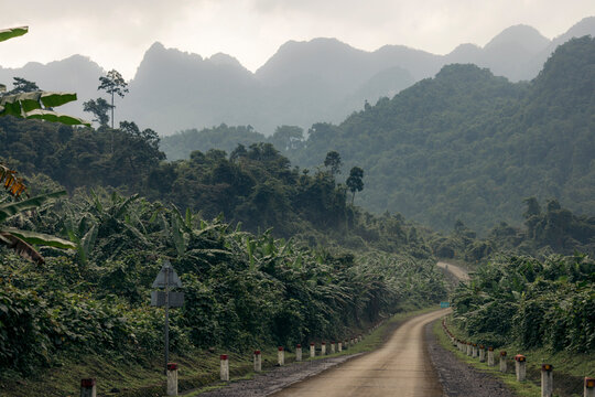 A winding road through lush green jungle and misty mountains under a cloudy sky. Son Trach, Bo Trach District, Quang B&Iuml;nh, Vietnam